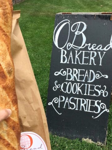 Chalkboard sign and loaf of bread on grass.
