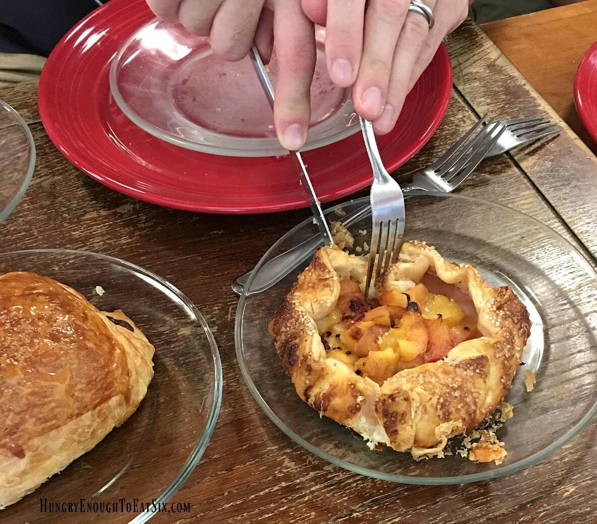 Hands using knife and fork to cut into a mini fruit gallette on a clear plate. 