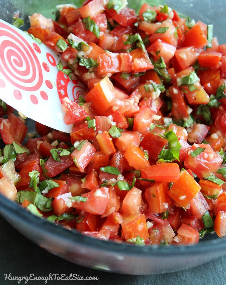 Large glass bowl with tomato salsa and basil and a rubber spatula