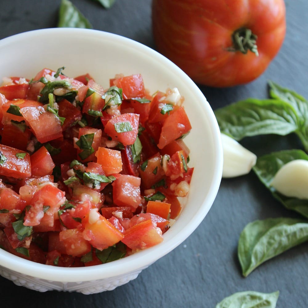 Chopped salsa with tomatoes and green basil in a white bowl