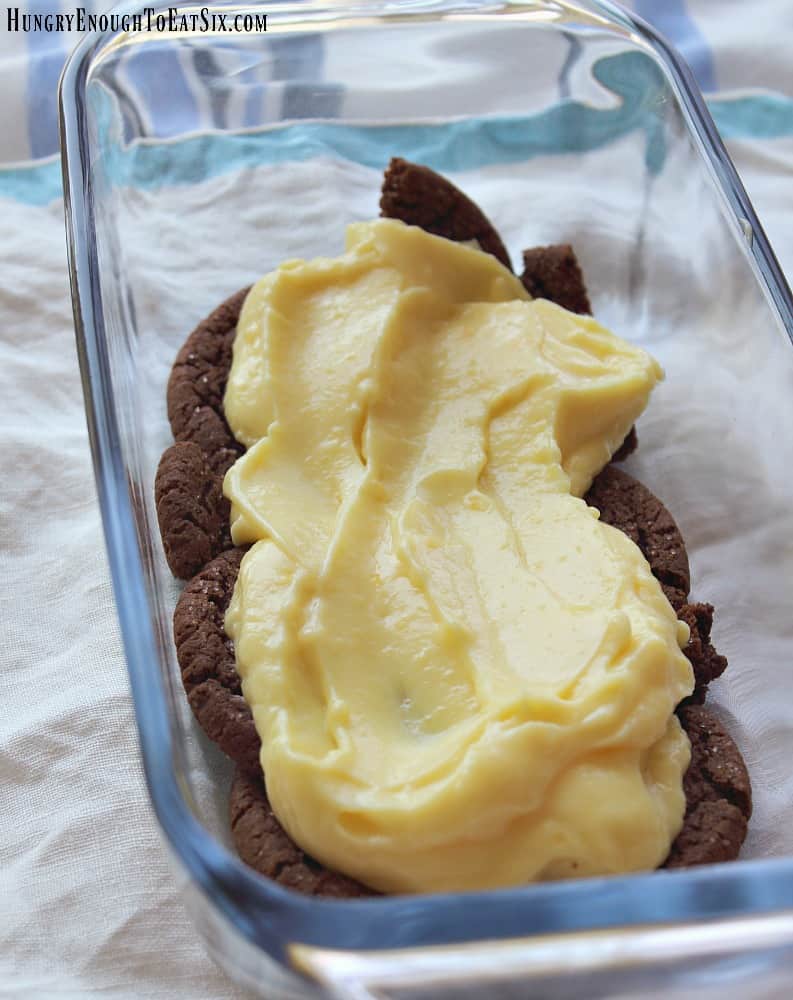 Vanilla pudding spread over chocolate cookies in a glass pan,