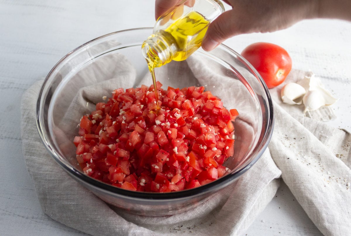 Olive oil pouring into bowl of diced tomatoes