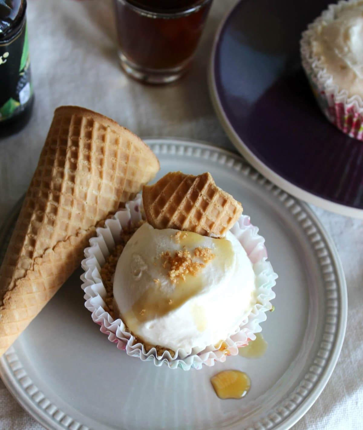A small grey plate with a mini icebox cake in a muffin wrapper with maple syrup and cone pieces on top.