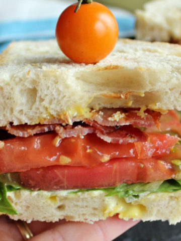 White bread sandwich with tomato and lettuce in a hand