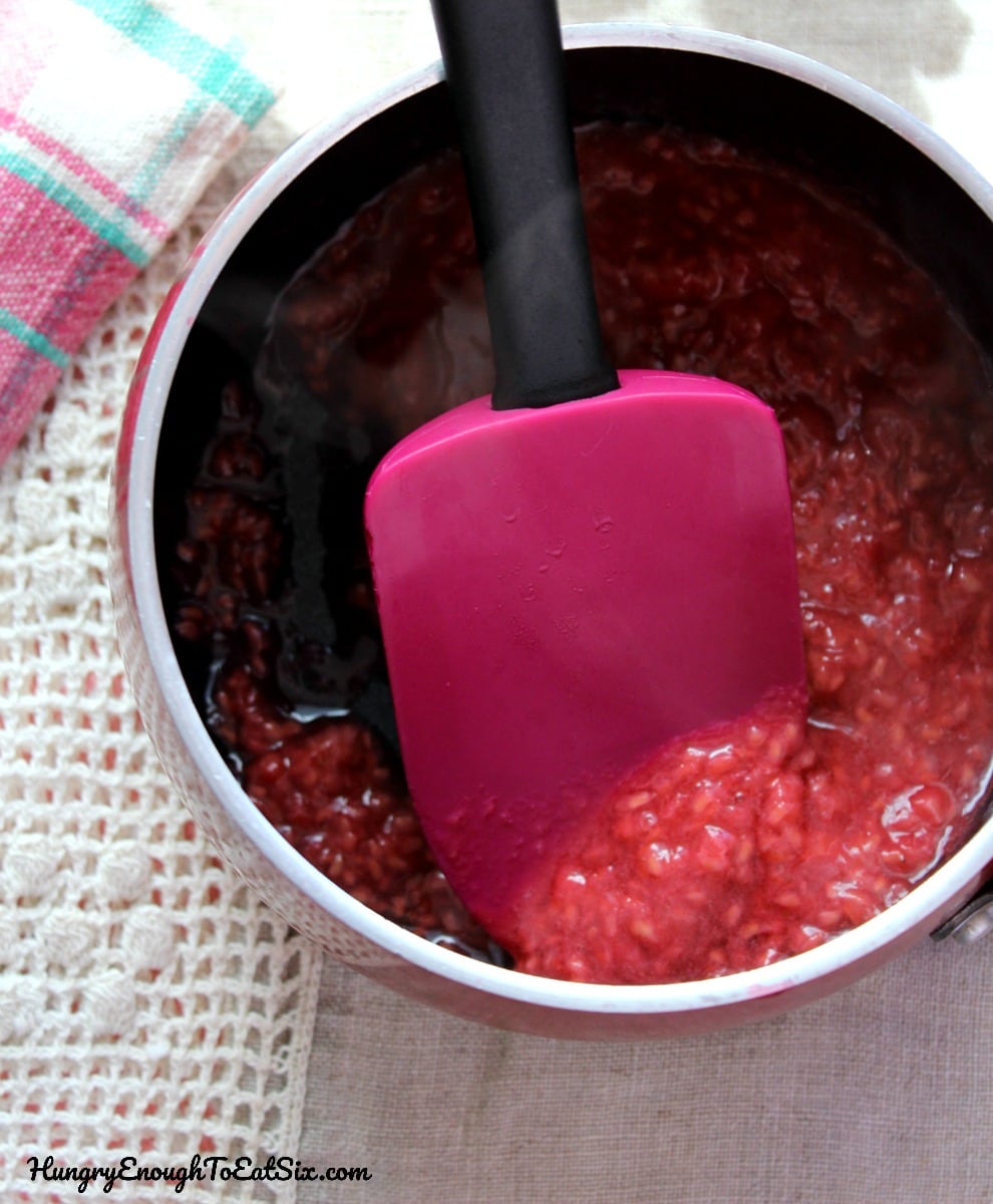 Small black pot with cooked raspberries and a rubber spatula.