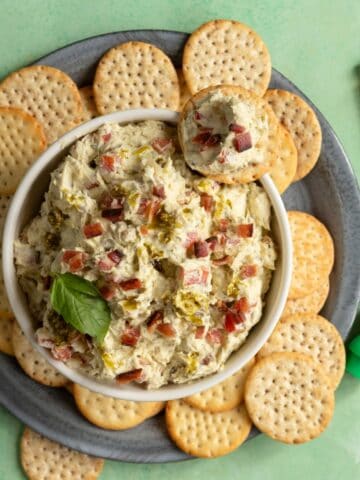 Platter of crackers with a bowl of cheese spread with bacon and pesto.