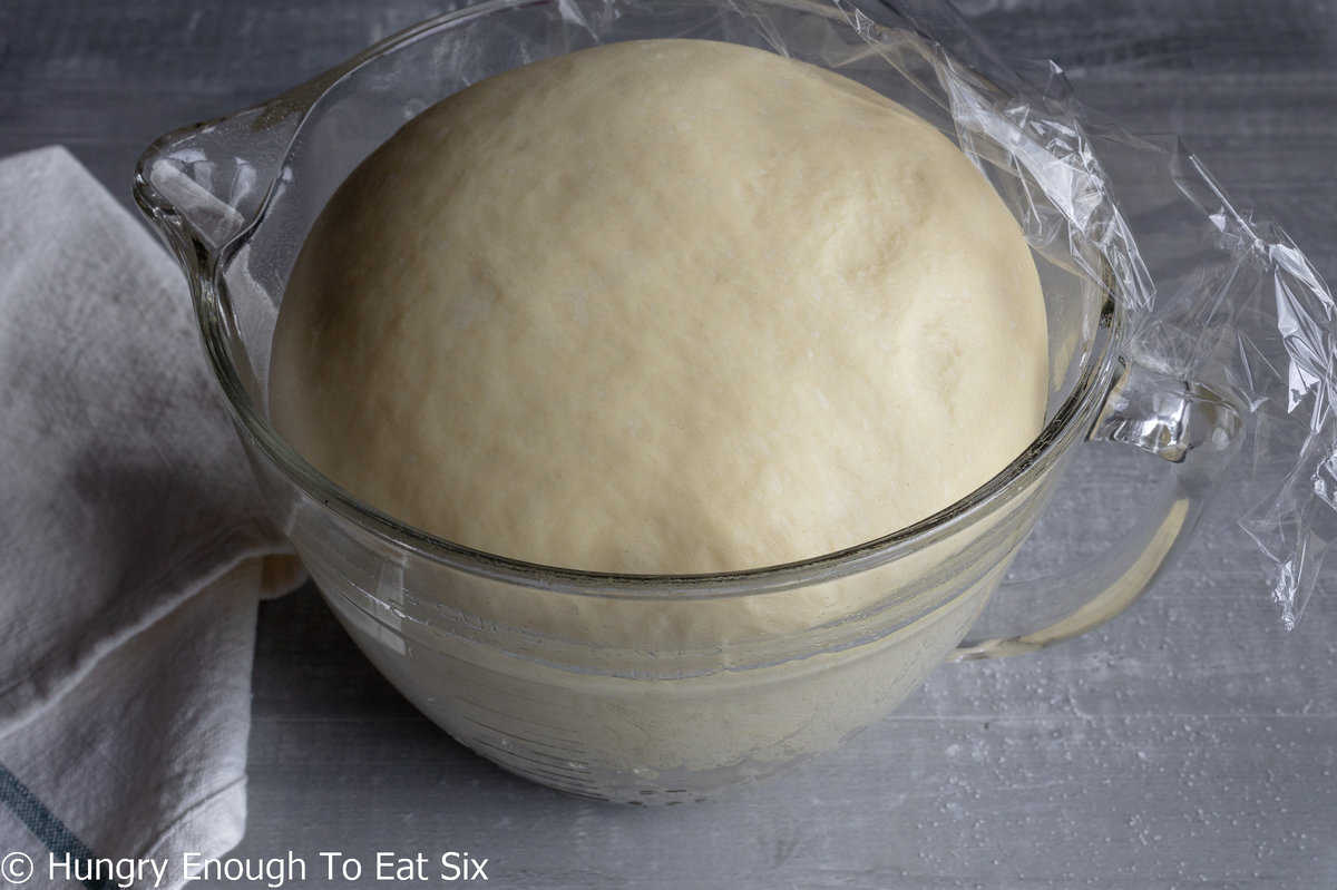 Risen bread dough in a glass bowl.