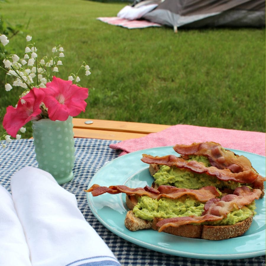 Plate of avocado toast on table next to a small vase of flowers
