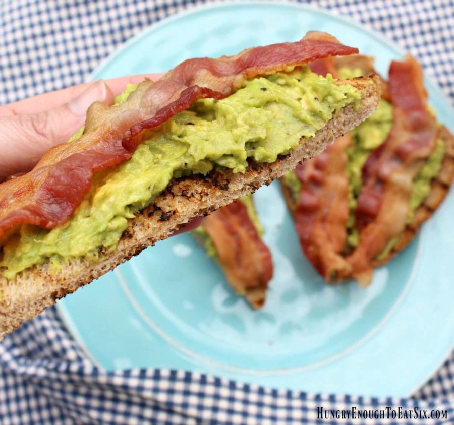 Diagonal slice of toast with avocado and bacon in a hand