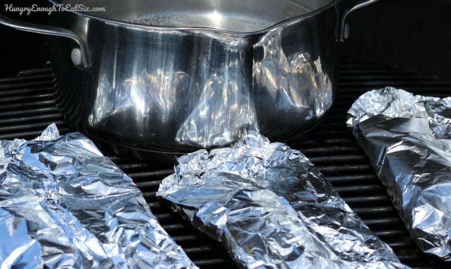 Foil packets and a silver pot on grill grates