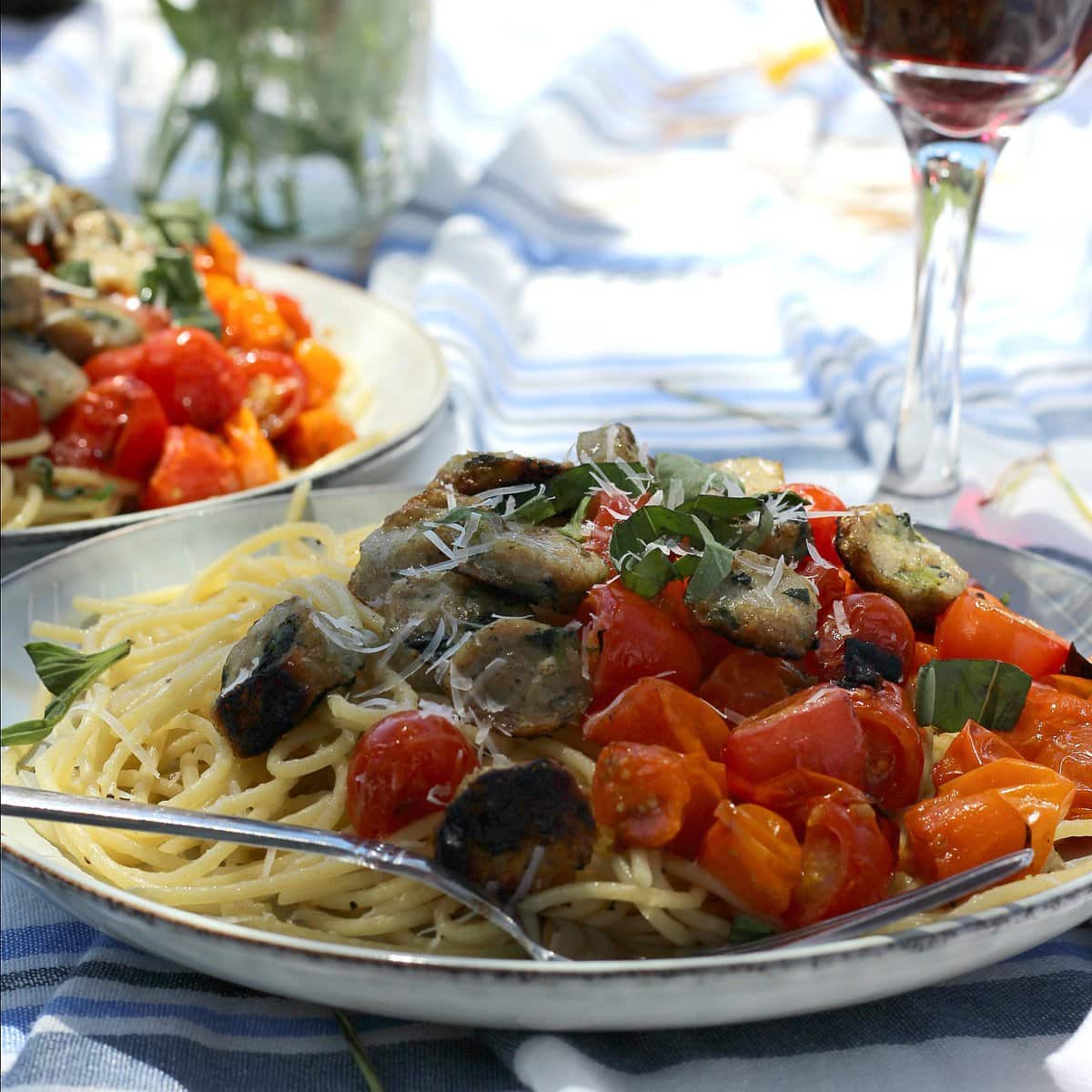 Outdoor table with a plate of pasta and tomatoes.