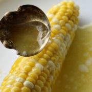 Cooked ear of corn being ladled with butter.