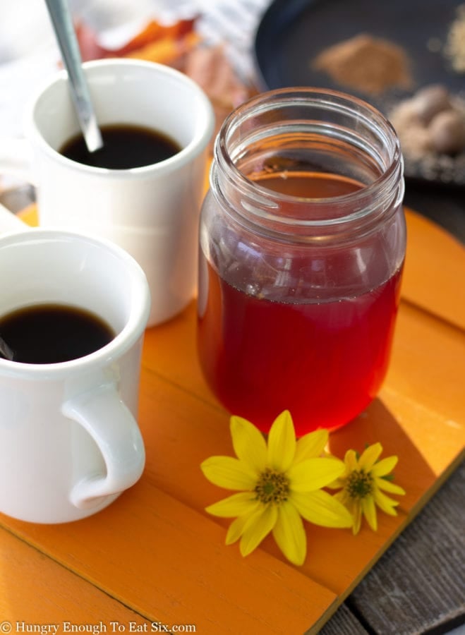 Cups of coffee with a jar of orange pumpkin syrup.