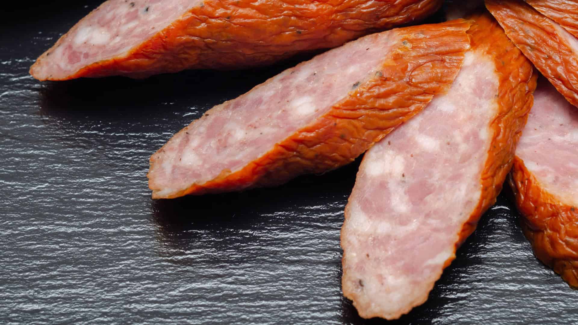 Slices of kielbasa on a dark table.