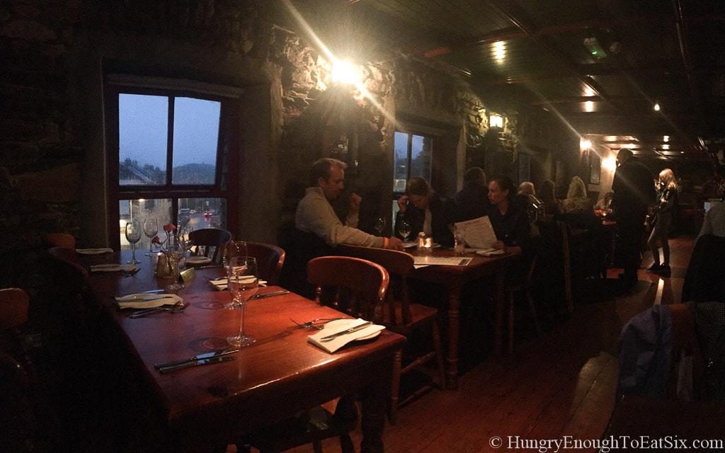 Dimly lit interior of pub and restaurant with people at tables.