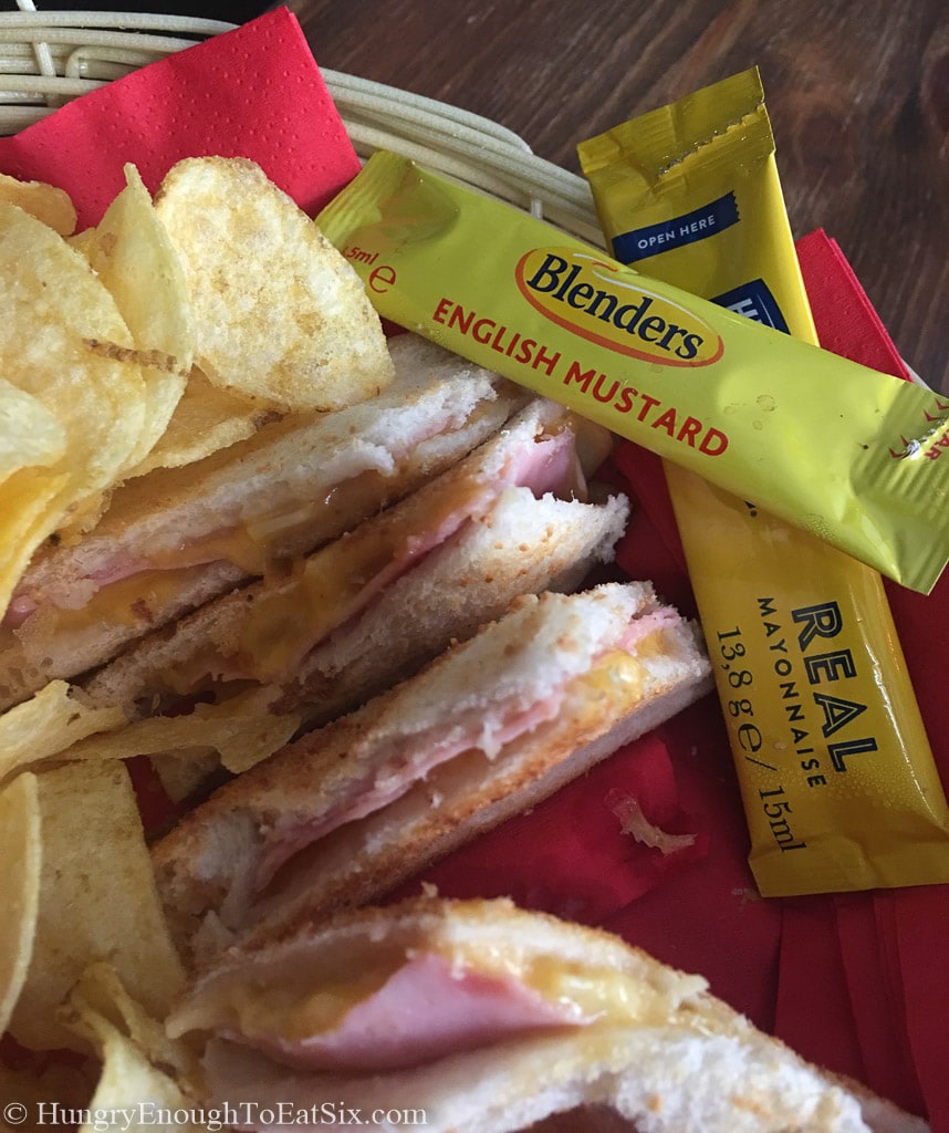 Grilled ham and cheese sandwich with chips and mustard.