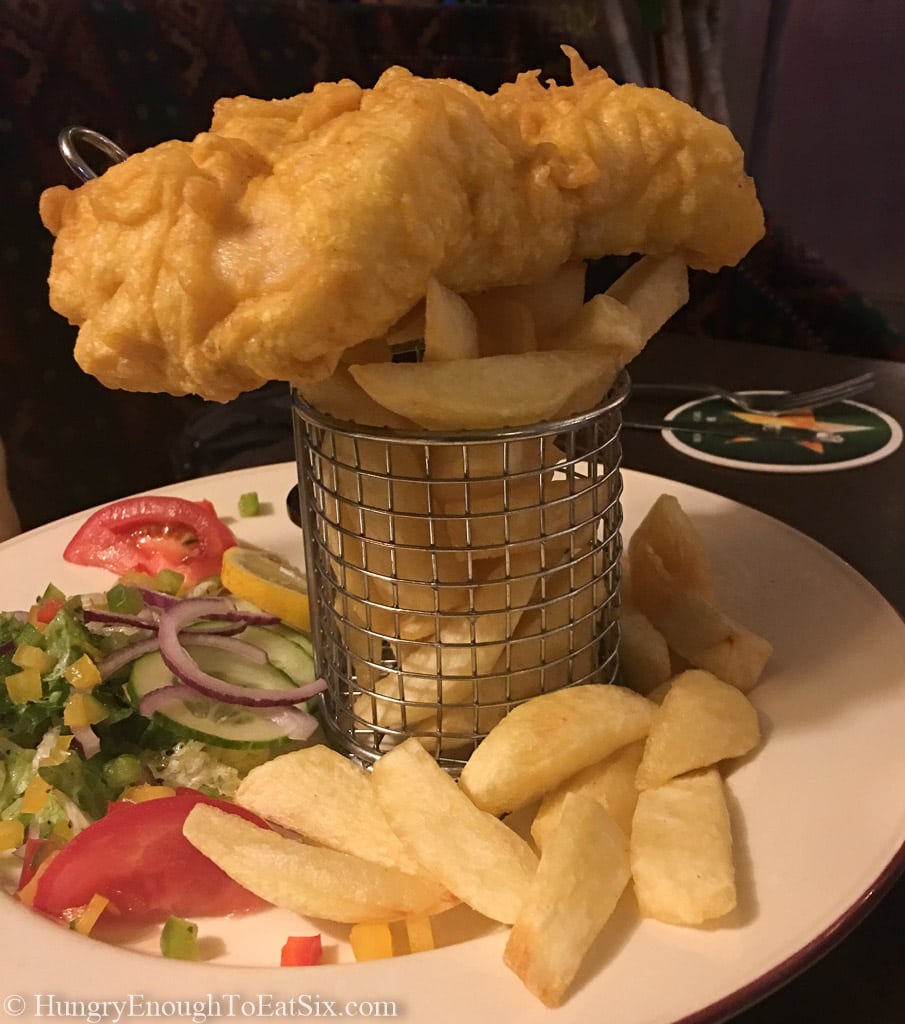 Battered Hake sitting on top of a basket of thick pub fries.  