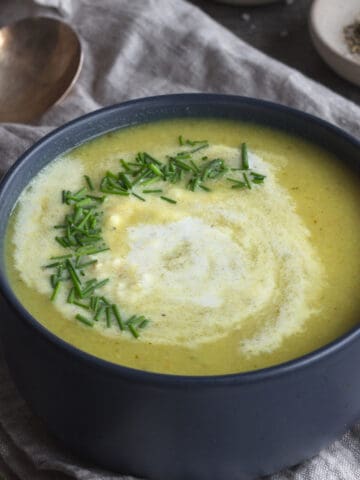 Bowl of yellowish soup with diced chives and cream