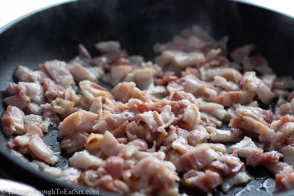 Chopped bacon cooking up in a pan.