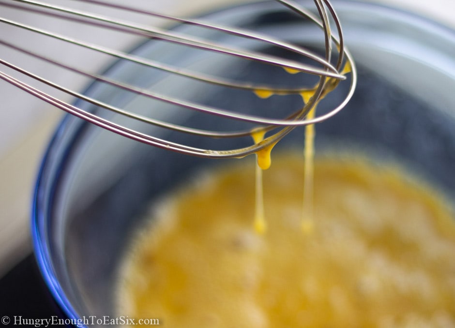Egg batter in a blue bowl and dripping from a whisk