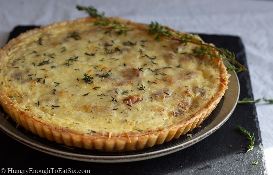 Baked quiche Lorraine on a gray plate with sprigs of fresh thyme.
