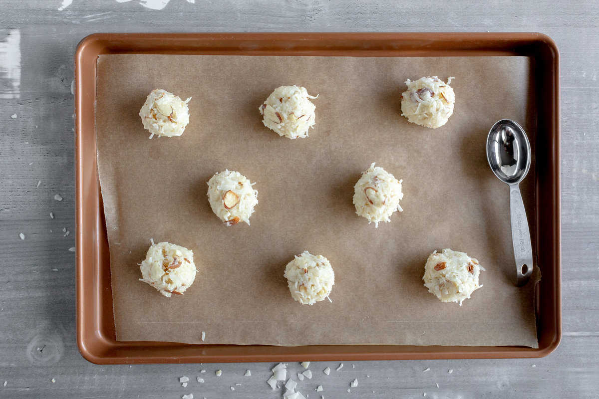 Mounds of almond coconut batter on a baking sheet.