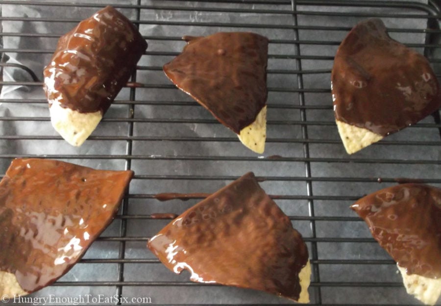 Several chocolate coated tortilla chips on a cooling rack.