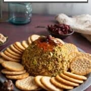 Pistachio-crusted cranberry cheese ball on plate with crackers.