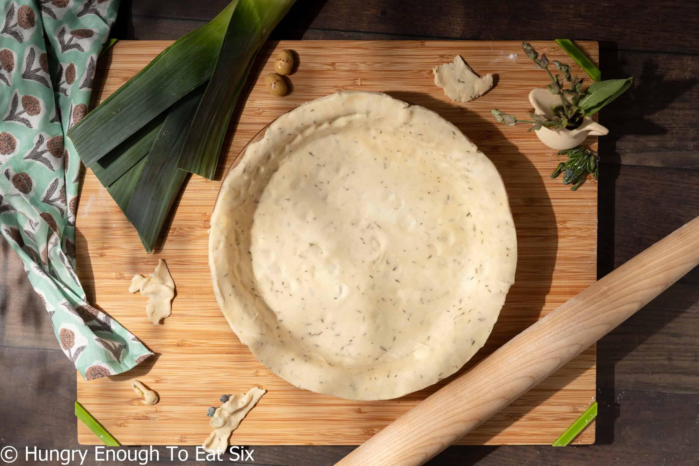 Herby pie shell in a glass pie plate with rolling pin nearby.