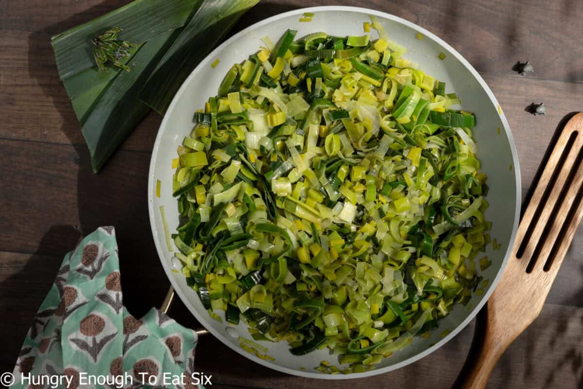 Sautéed sliced leeks in a skillet, cooked to go into a leek and potato pie.