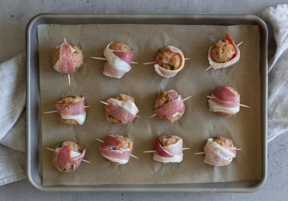 Bacon wrapped raw meatballs on a baking sheet