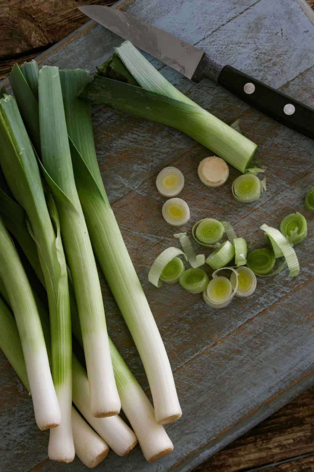 Several tall green and white fresh leeks, some sliced to prepare for a leek and potato pie.