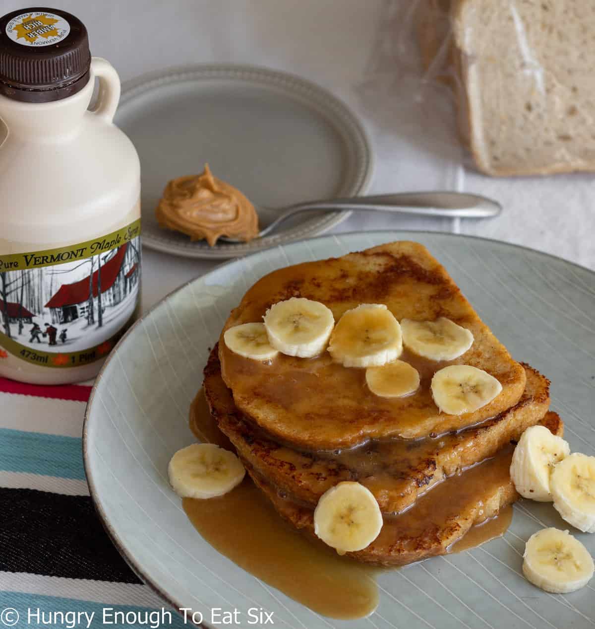 Jug of maple syrup with French toast and sliced bananas.