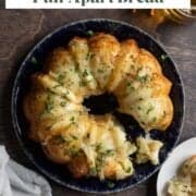 Baked tear-and-share bread made with garlic and cheese, and topped with fresh herbs, on a blue plate.