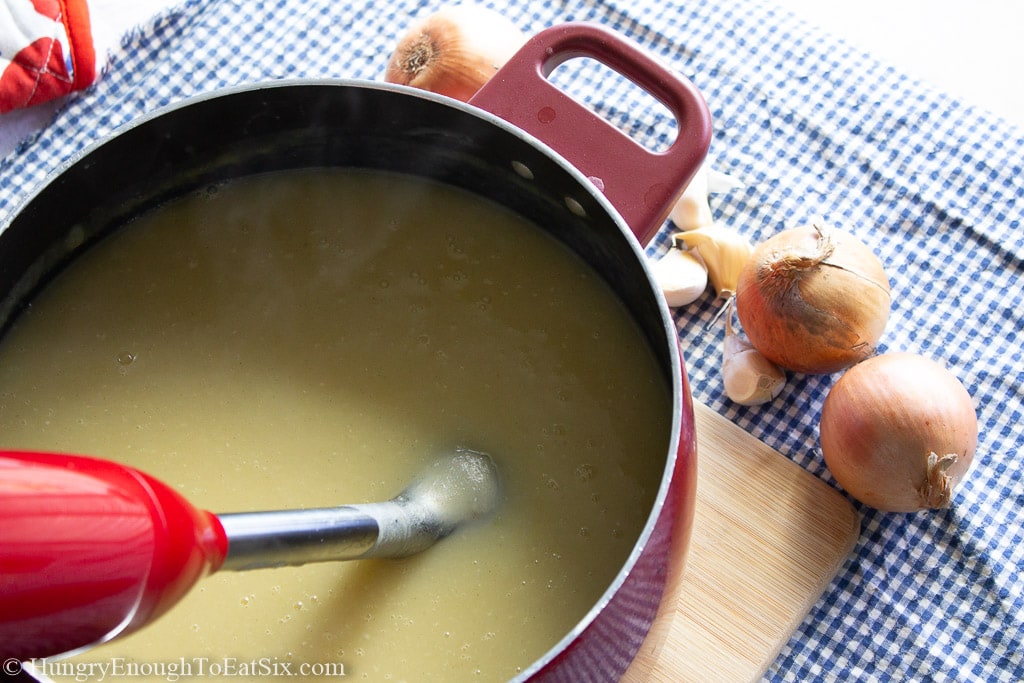 Red pot holding soup with an immersion blender