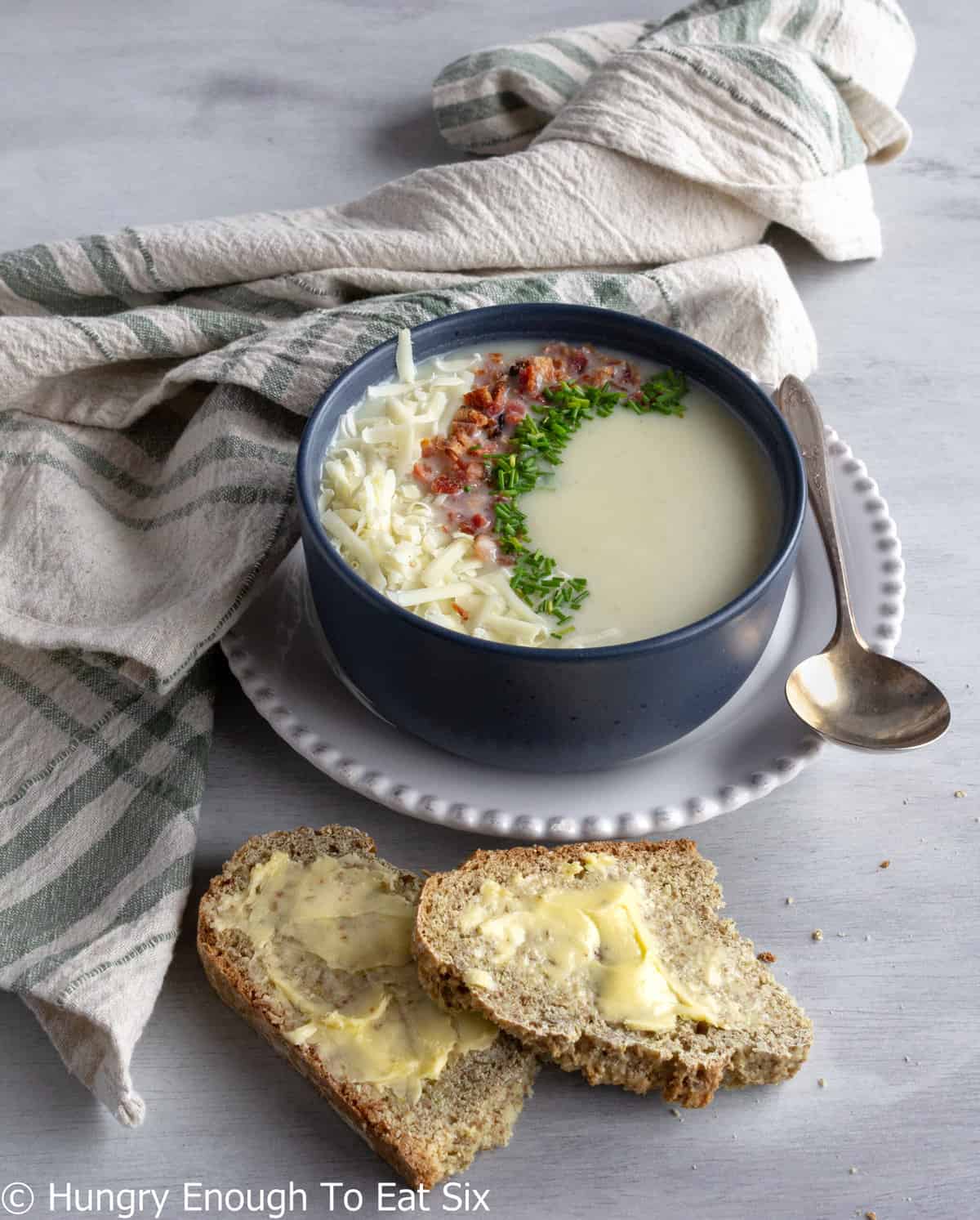 Bowl of creamy soup with toppings and two slices of buttered bread.