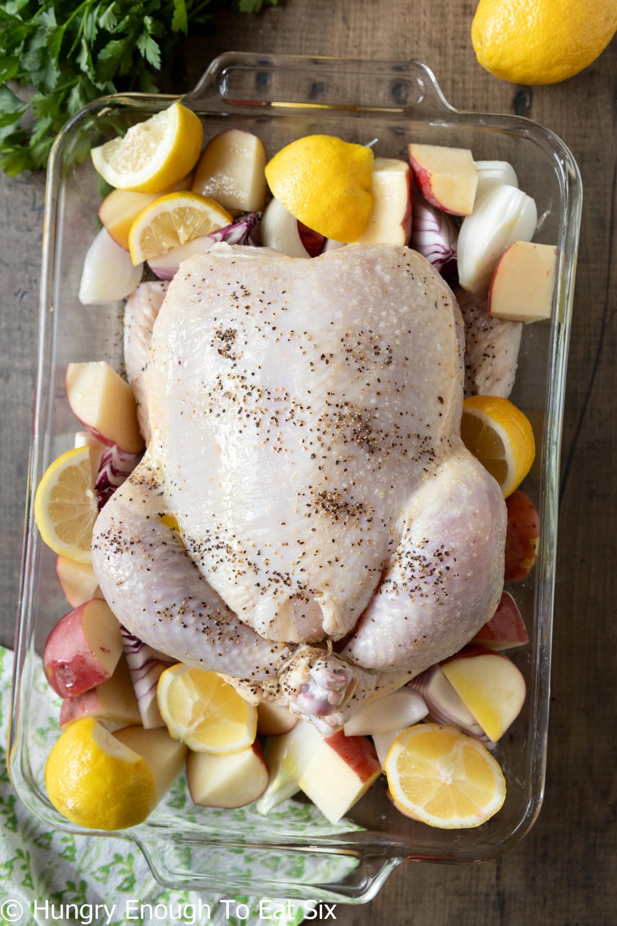 Whole chicken in a baking dish with lemons and potatoes.