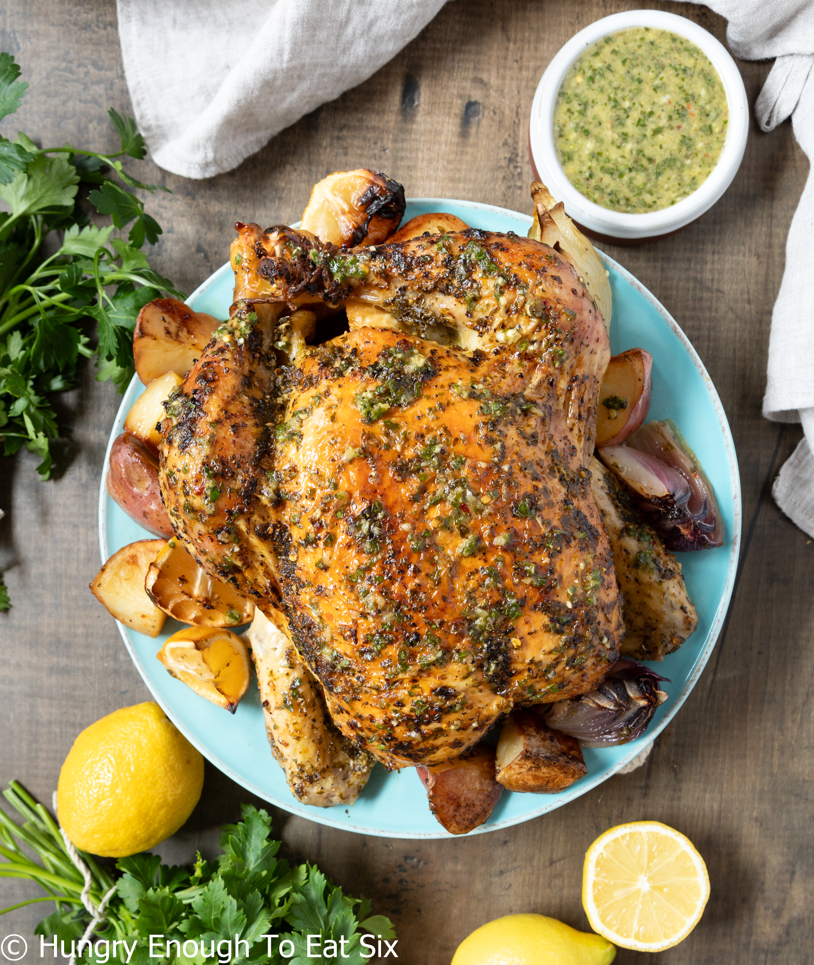 Whole roasted chicken on a blue plate with fresh herbs nearby.