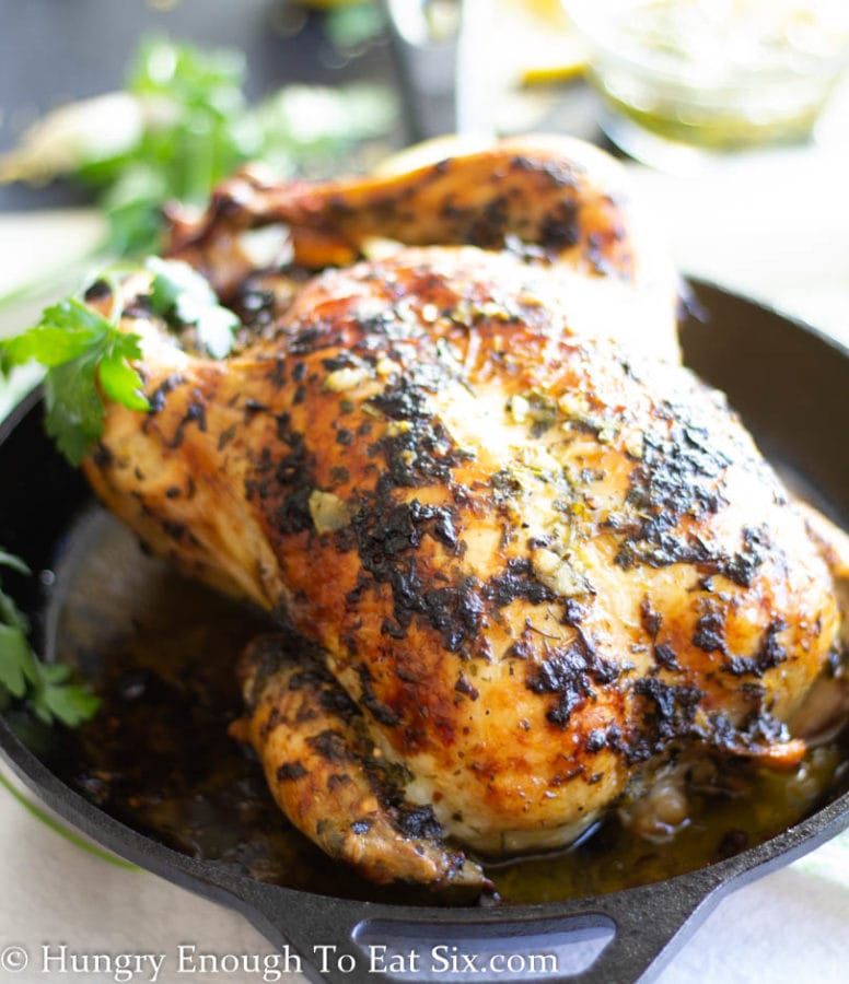 View of a roasted chicken with chimichurri sauce in a cast iron skillet.