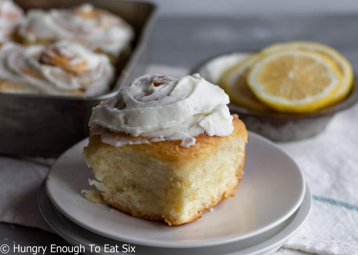 Icing-topped lemon roll on white plate.