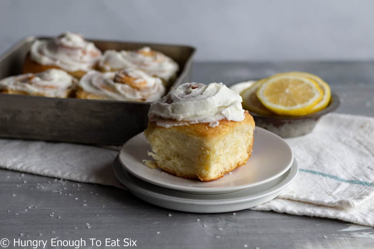 Frosted lemon rolls in pan and one on a plate.