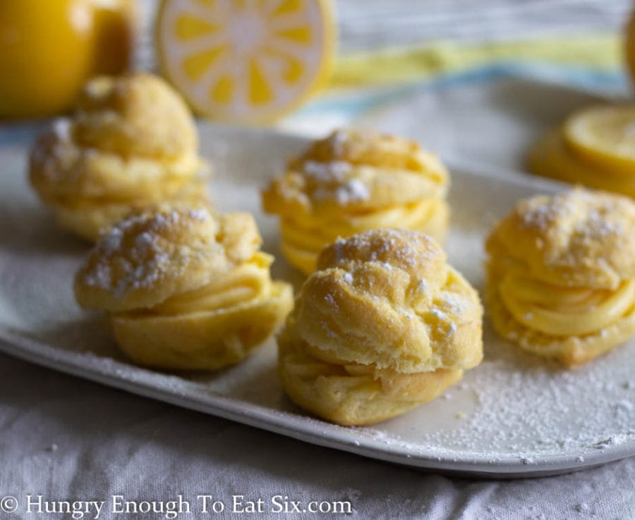 Cream puffs filled with lemon pastry cream on a white plate dusted with confectioner's sugar