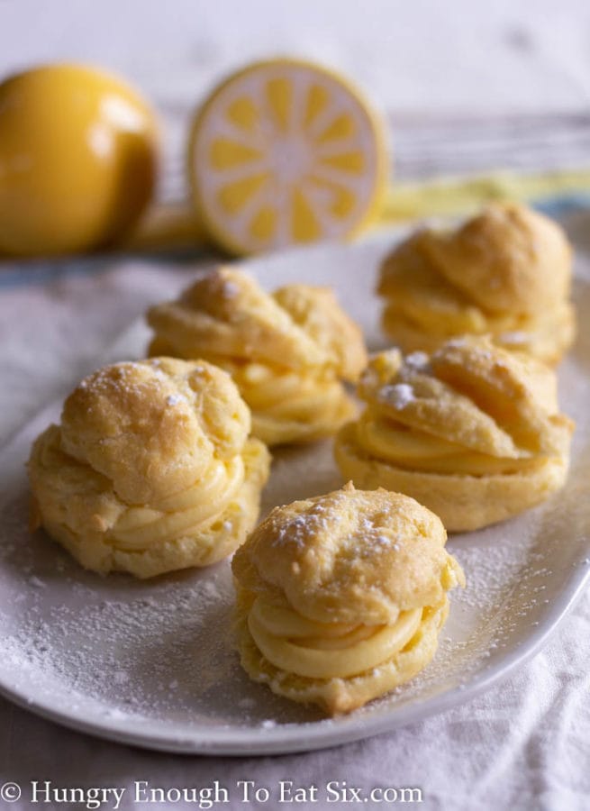 Vertical image of filled cream puffs on a white plate dusted with confectioner's sugar