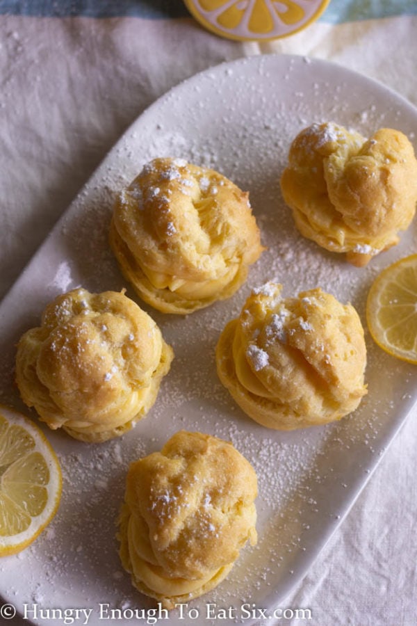 Vertical image of filled cream puffs on a white plate dusted with confectioner's sugar