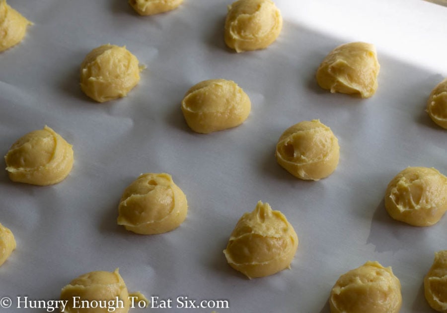 Mounds of choux pastry dough lined up on a baking sheet.