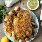 Herb coated roasted chicken on a blue plate with dish of green herb sauce nearby.