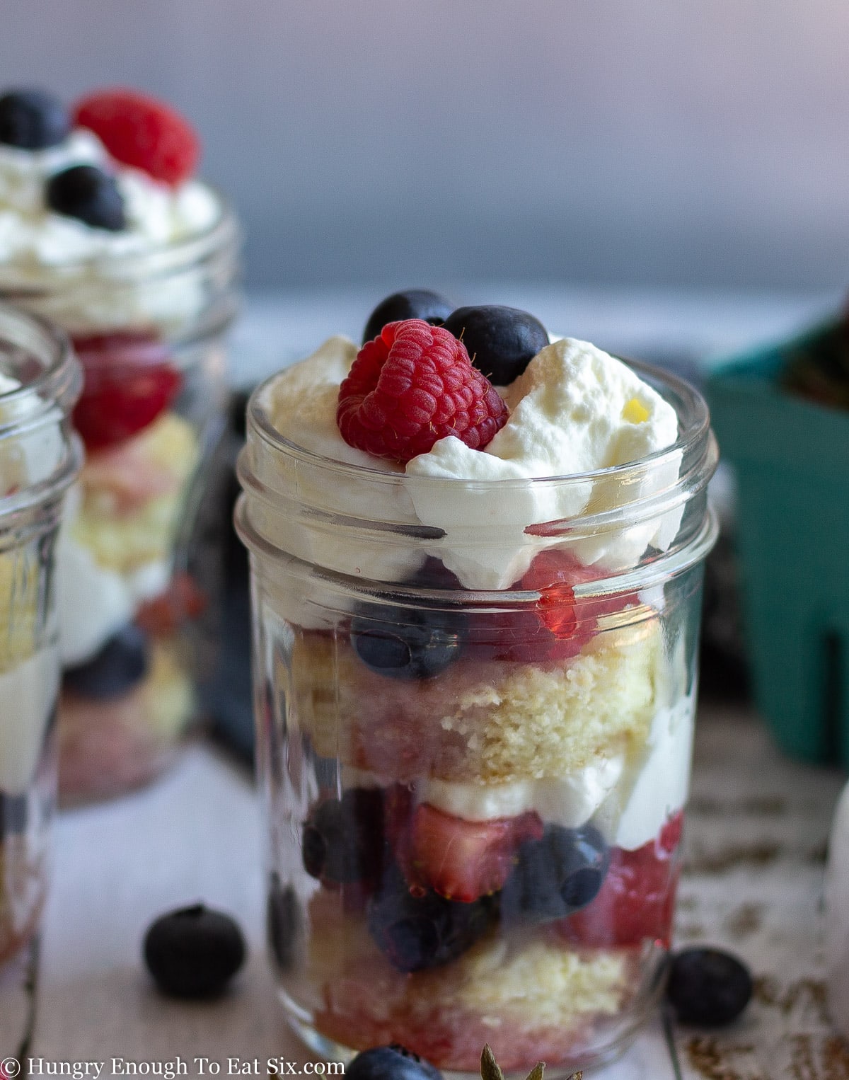 Trifle of cream, shortcake, and berries in a clear jar.
