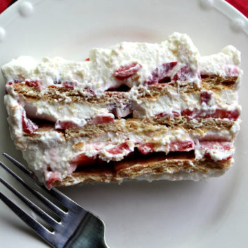 Fork and white plate holding a slice of strawberries and cream icebox cake.