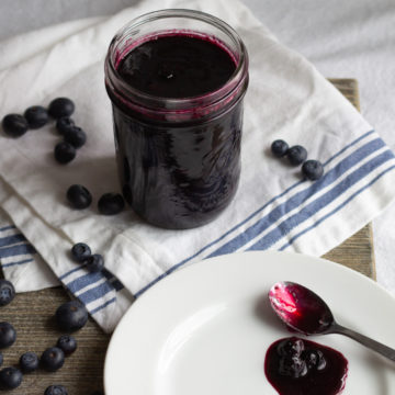 Blueberry sauce in a jar and on a spoon lying on a plate.