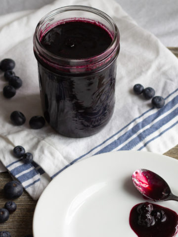Blueberry sauce in a jar and on a spoon lying on a plate.